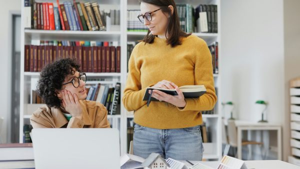 two women are architects, working on a laptop and talking while doing a creative assignment or cours