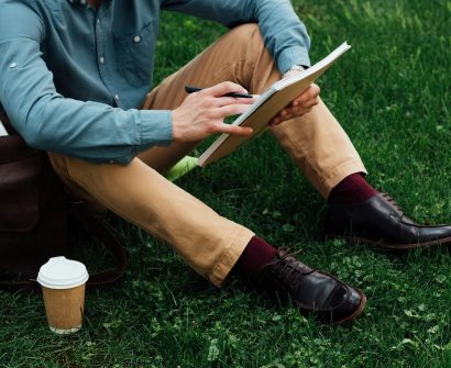 cropped shot of young man writing in notebook while sitting on grass